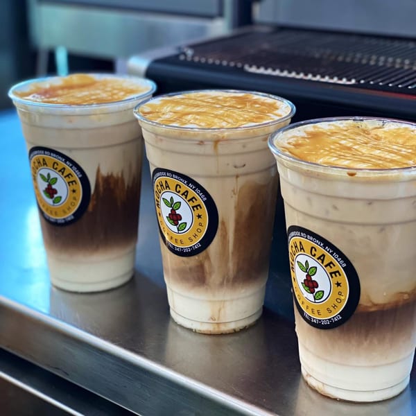 Three Mocha Cafe iced coffees with caramel drizzle on a metal counter.