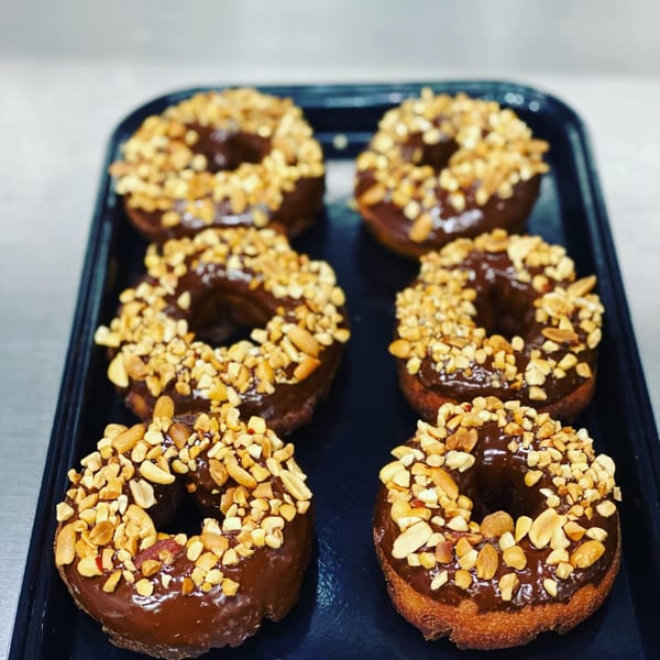 Six chocolate-glazed donuts topped with chopped peanuts on a dark tray at Mocha Cafe.